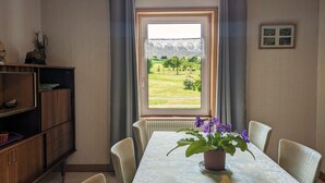 A dining room with a table set for four, a potted plant on the table, and a view of a green landscape through a window. - Charming Mountain View Cottage Near Gérardmer: Spacious, Cozy, Garden, Parking, Ideal for Hikes (Jussarupt)