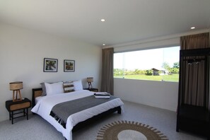 Une chambre avec un grand lit, deux tables de chevet, une fenêtre donnant sur un beau paysage et une porte.