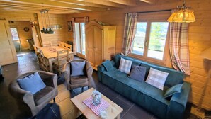 A cozy cabin interior with a wooden dining area, a sofa, and a table with a vase and glass. - Comfortable chalet with terrace and wood stove, pets allowed (Le Tholy)