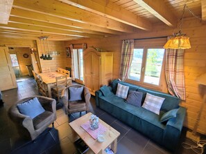 Un acogedor interior de cabaña con un comedor de madera, un sofá y una mesa con un florero y vaso.