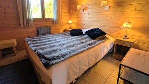 A wooden cabin bedroom with a bed, two bedside lamps, a window with curtains, and a chair. - Comfortable chalet with terrace and wood stove, pets allowed (Le Tholy)