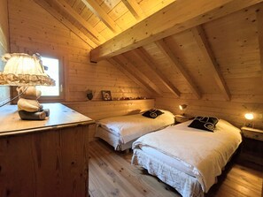 Une chambre mansardée chaleureuse, avec deux lits, un bureau et une lampe.