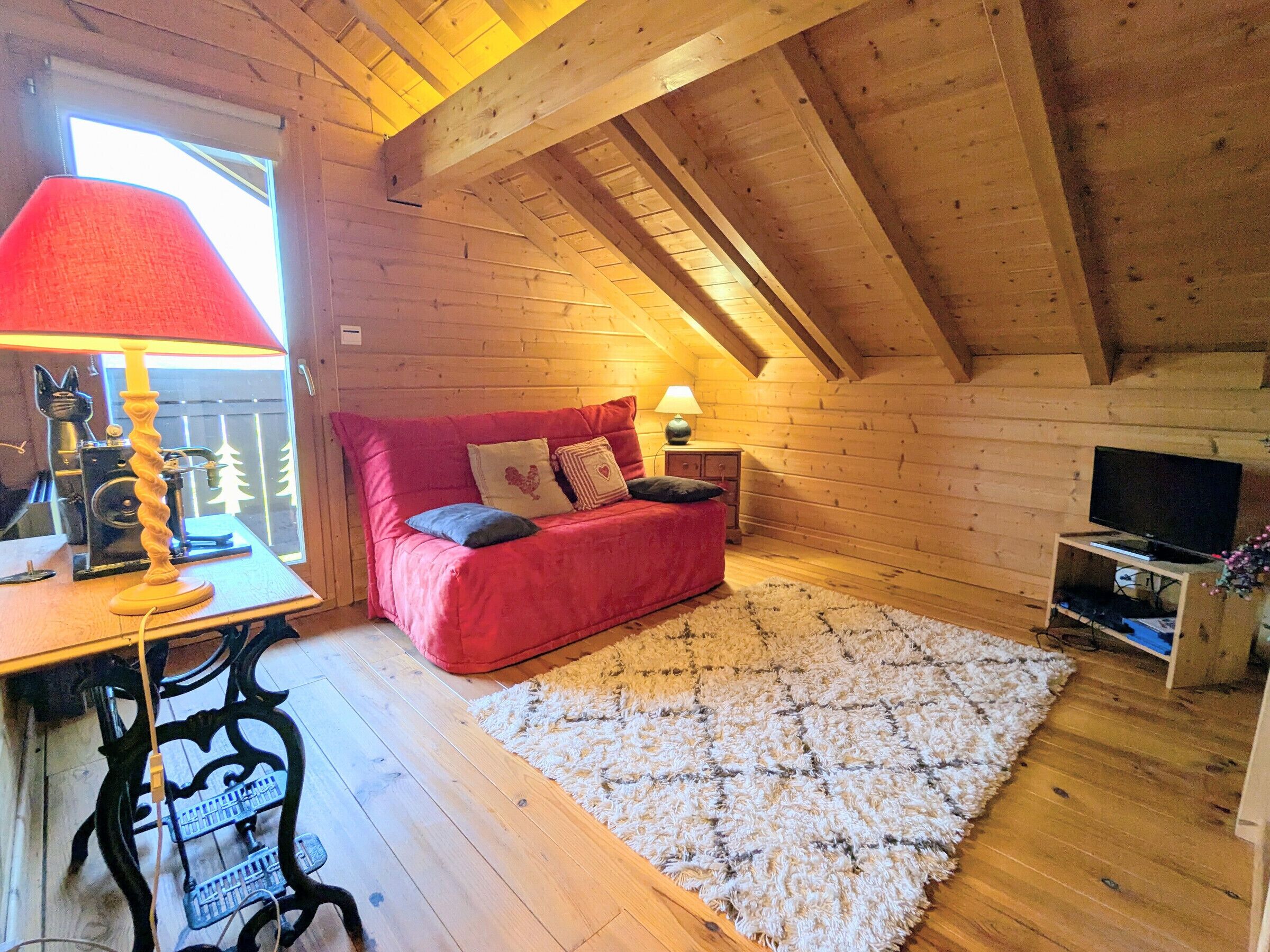 Ein gemütliches Blockhaus mit Holzvertäfelung, einem roten Sofa, einem kleinen Tisch mit Lampe und einem Fernseher auf einem Holzboden.