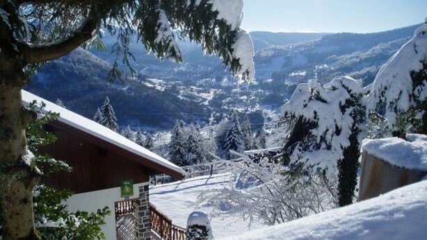 A snow-covered mountain landscape with a wooden cabin and a snow-covered tree in the foreground.