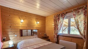 A wooden cabin bedroom with a bed, bedside tables, a mirror, and a window with curtains.