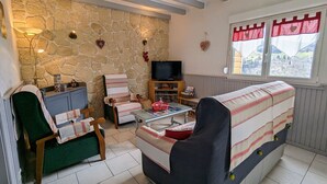A cozy living room with a stone wall, a sofa, a chair, a small table, and a television.