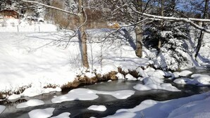 A snow-covered landscape with a frozen stream, trees, and a distant building.