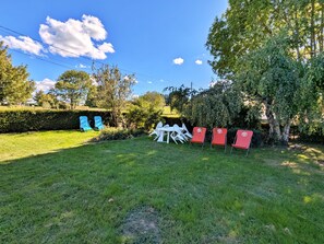 A grassy outdoor area with a seating arrangement consisting of white and red chairs, a white table, and a hedge in the background.