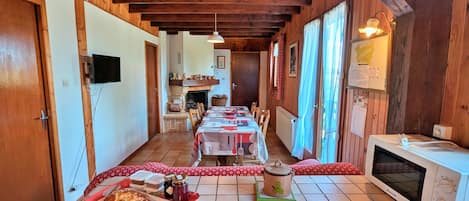 Un coin repas chaleureux avec une longue table dressée pour le repas, un four à micro-ondes et une cheminée en arrière-plan.