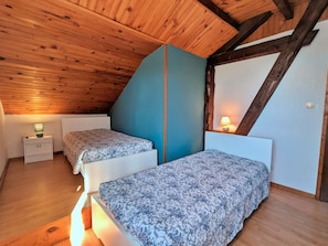 A room with two beds, wooden ceiling beams, and a sloped ceiling.