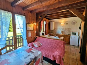 A cozy cabin interior with a dining area, a kitchen with basic appliances, and a view of the outdoors.