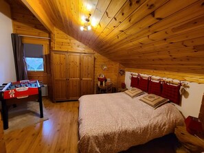 A cozy room with a bed, wooden ceiling, and a foosball table. - Luxury Chalet with Sauna, WiFi, Private Terrace & Garden Near Vosges Mountains (Saint-Nabord)