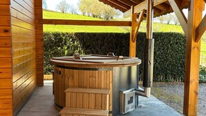 Puinen sauna, jossa on penkki ja portaat, metallinen kiuas ja näkymä vehreään maisemaan.