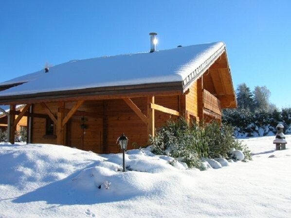 Una cabaña de madera con techo nevado, chimenea y porche cubierto.