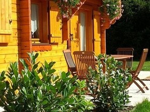 A wooden cabin with a porch, outdoor seating, and greenery. - Luxury Chalet with Sauna, WiFi, Private Terrace & Garden Near Vosges Mountains (Saint-Nabord)