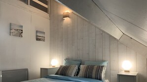 A bedroom with a sloped ceiling, a bed with blue bedding, two bedside lamps, and a small nightstand.