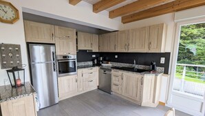 A modern kitchen with wooden cabinets, stainless steel appliances, and a large window offering a view of greenery. - Spacious cottage with all comforts, Vosges (Anould)