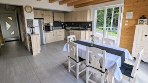A spacious kitchen with wooden cabinets, a dining area with a table and chairs, and a view of greenery outside. - Spacious cottage with all comforts, Vosges (Anould)