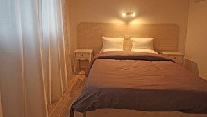 A bedroom with a wooden headboard, two bedside tables, a bed with a brown bedspread, and a wall-mounted light fixture. - Spacious cottage with all comforts, Vosges (Anould)