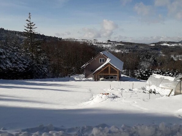 Une cabane au toit en pente, entourée d’arbres couverts de neige et sous un ciel dégagé.