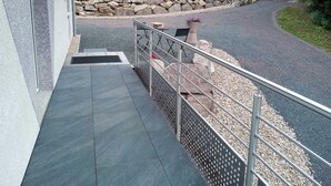 A modern outdoor staircase leading to a patio area with a stone wall and a gravel path. - Spacious cottage with all comforts, Vosges (Anould)