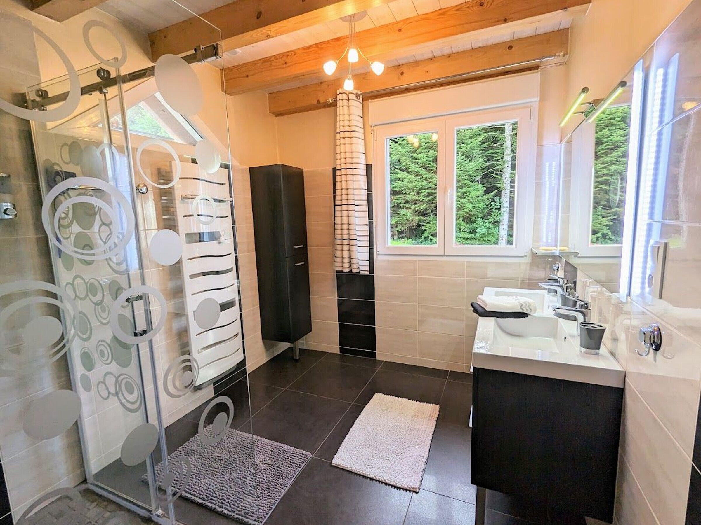 A modern bathroom with a shower, a sink, and a window with a view of greenery.