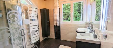 A modern bathroom with a shower, a sink, and a window with a view of greenery.