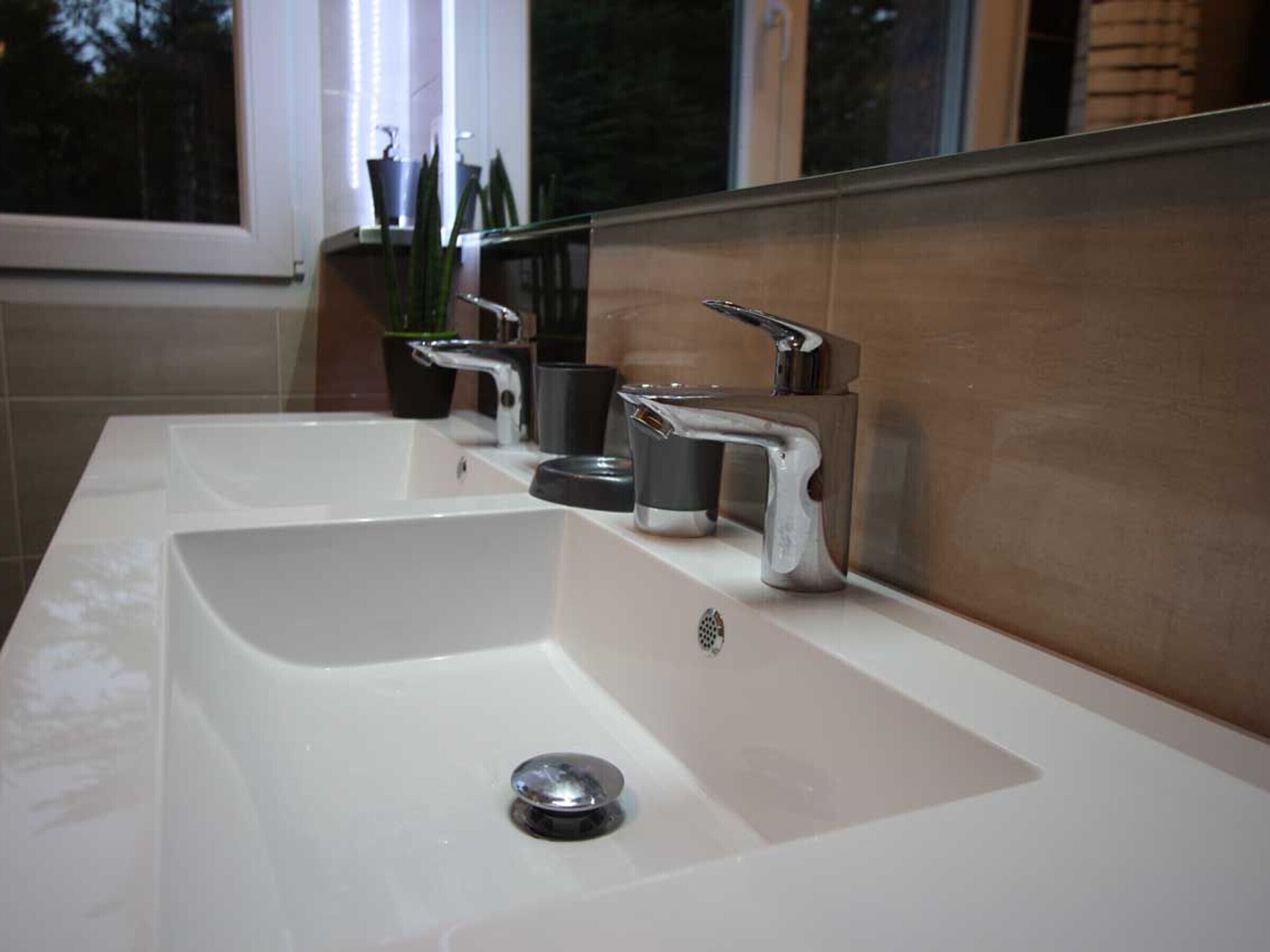 Une salle de bain moderne avec un lavabo blanc, deux robinets et un miroir.