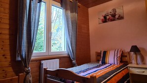 Une chambre à coucher dans une cabane en bois, avec un lit, une table de chevet, une lampe et une fenêtre avec des rideaux.