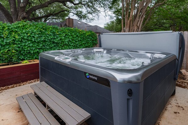 Ein Whirlpool mit Sitzbank davor, umgeben von viel Grün.