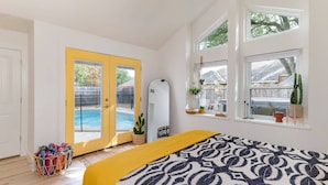 A bedroom with a bed, a yellow door, a window with plants, and a view of a swimming pool. - Remodeled, Private Pool & Hot Tub, Gas BBQ, Xbox, Ping Pong, Foosball, Fully-equipped Kitchen (Round Rock)