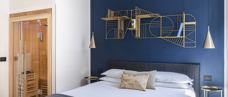 Une chambre d’hôtel moderne avec un grand lit, une décoration murale aux motifs géométriques, une armoire à portes en verre et une table de chevet avec une lampe.