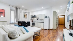 Quarto de hotel moderno com uma cama, uma kitchenette pequena, área de refeições e um corredor que leva a uma porta.