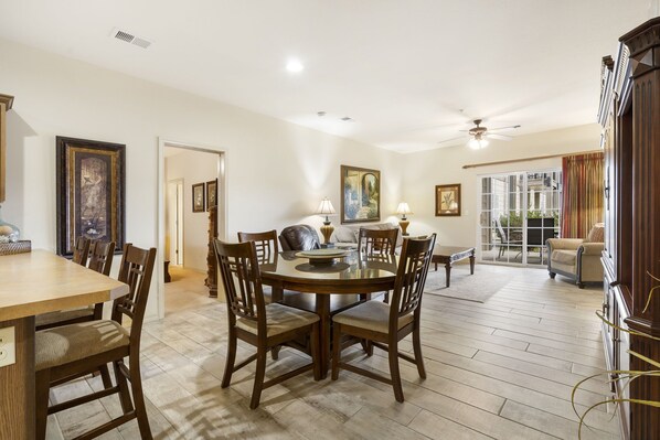 A dining area with a round table and chairs, a sofa, and a view of the outdoors through a glass door.