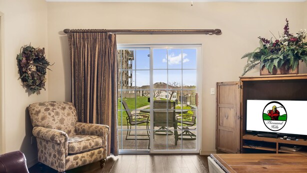 A living room with a sliding glass door leading to a patio, a floral armchair, a wooden coffee table, and a television on a wooden stand. - Walk-in 2 King Bedroom, 2 Bath Golf Condo with Covered Patio - Walk out to Pool! (Branson)
