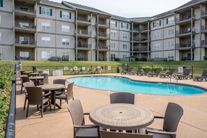 A multi-story residential building with balconies, a swimming pool, outdoor seating, and a fenced patio area.