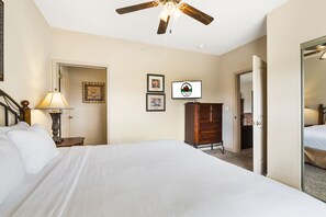 A hotel room with a large bed, a ceiling fan, a dresser, and a television.