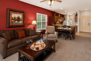 A living room with a red wall, a sofa, a coffee table with snacks, and a dining area with a table and chairs. - Pool View 3BR Condo Near Branson Strip • Walk-In • Golf Course Location • Sleeps 8 (Branson)