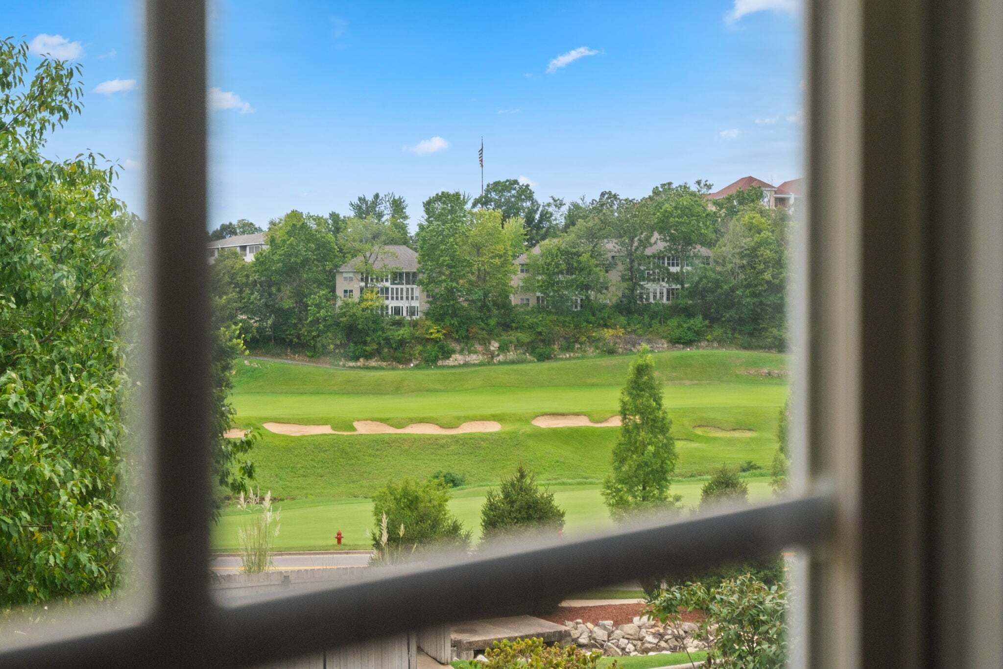 A view of a golf course with sand bunkers and a flagstick, surrounded by trees and residential buildings.