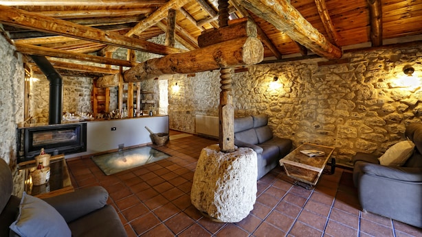 Un interior rústico con vigas de madera a la vista, paredes de piedra, una chimenea y asientos cómodos.