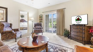 A spacious living room with a ceiling fan, a large window with curtains, a television, and a fireplace. - 2 Bedroom, 2 Bath Golf Condo with Private, Covered Patio (Branson)
