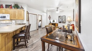 A modern kitchen with wooden cabinets, a microwave, and a coffee maker. There is a dining area with a glass table and chairs, and a ceiling fan. - Branson Condo Near Attractions • Pool Access • Sleeps 4 (Branson)