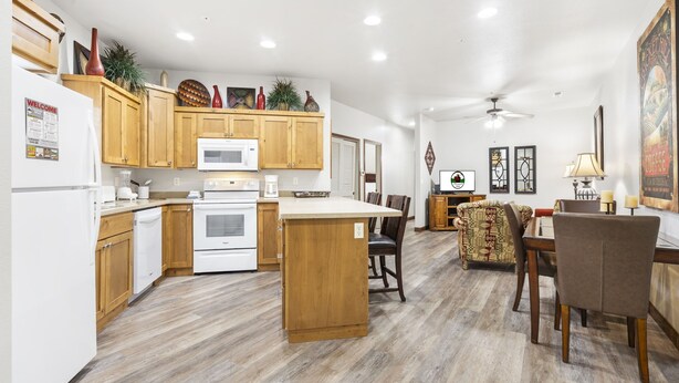 A modern kitchen with wooden cabinets, a central island, and a dining area with a patterned sofa and wooden table. - Branson Condo Near Attractions • Pool Access • Sleeps 4 (Branson)