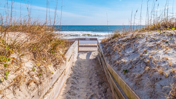 A wooden pathway leading to a beach with a wooden railing on one side. - Cottage at Scotch Bonnet | Walk to the Beach! (Carolina Beach)