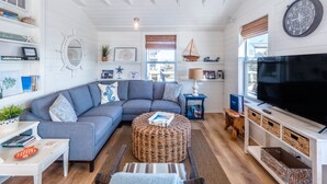 A modern living room with a grey sectional sofa, a woven ottoman, a flat-screen TV, and nautical decor. - Cottage at Scotch Bonnet | Walk to the Beach! (Carolina Beach)