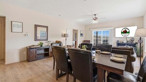 Uma área de refeições com mesa de madeira, cadeiras pretas e ventilador de teto.