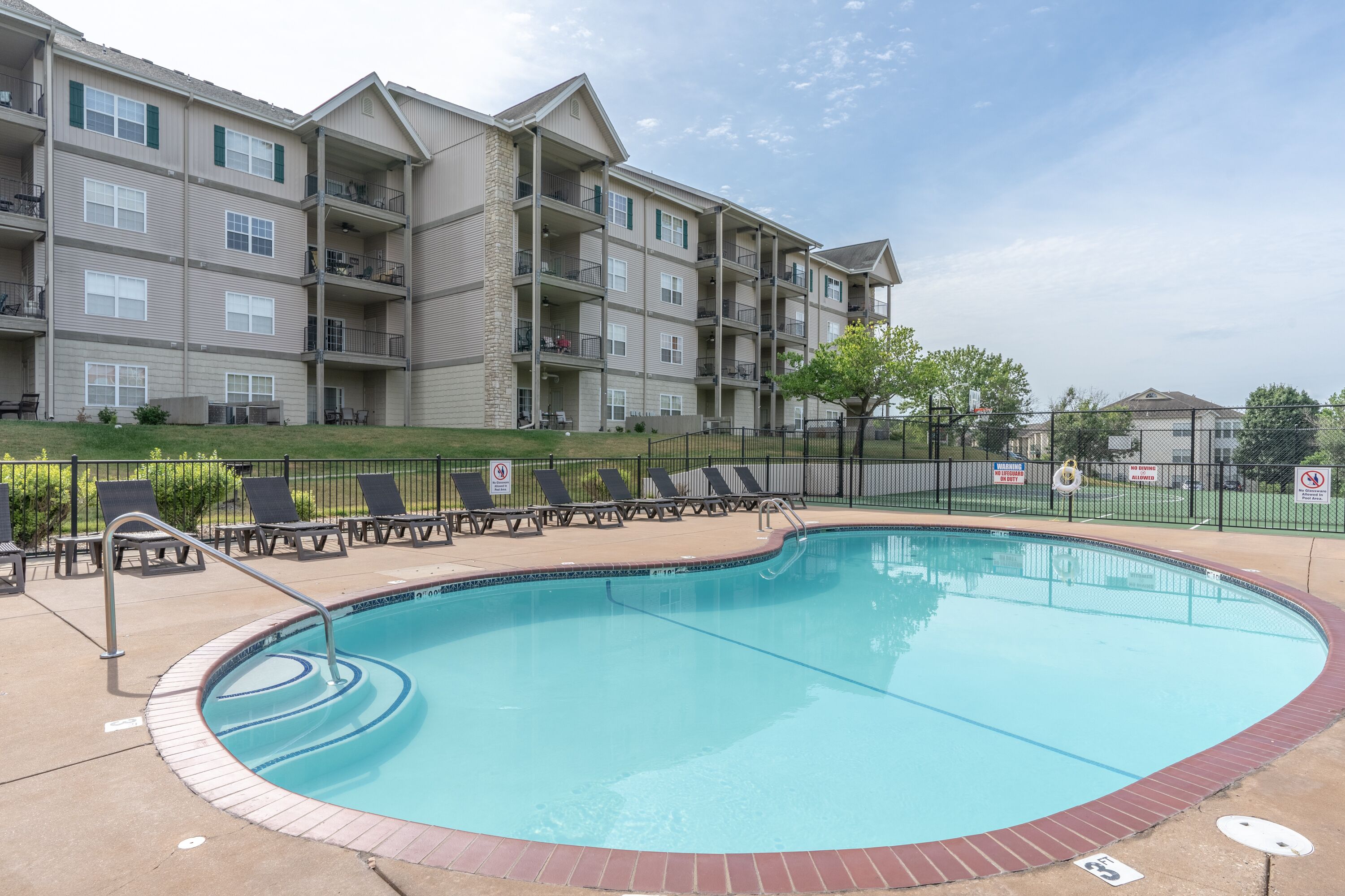 A swimming pool with lounge chairs and a building with multiple balconies in the background.