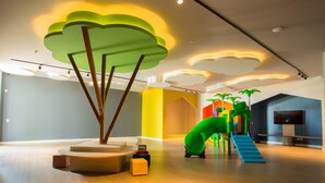 Ein moderner Indoor-Spielbereich mit Rutsche, Klettergerüsten und einem Fernseher an der Wand.