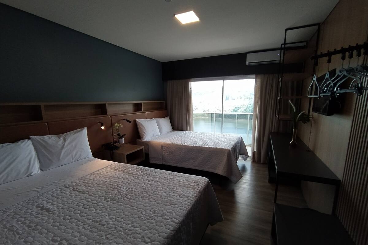 A hotel room with two beds, a nightstand, a desk, and a large window with curtains.