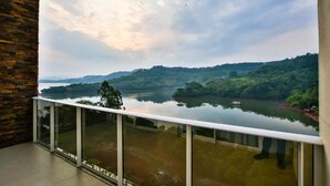 Ein Balkon mit Glasgeländer mit Blick auf einen stillen See und grüne Hügel.